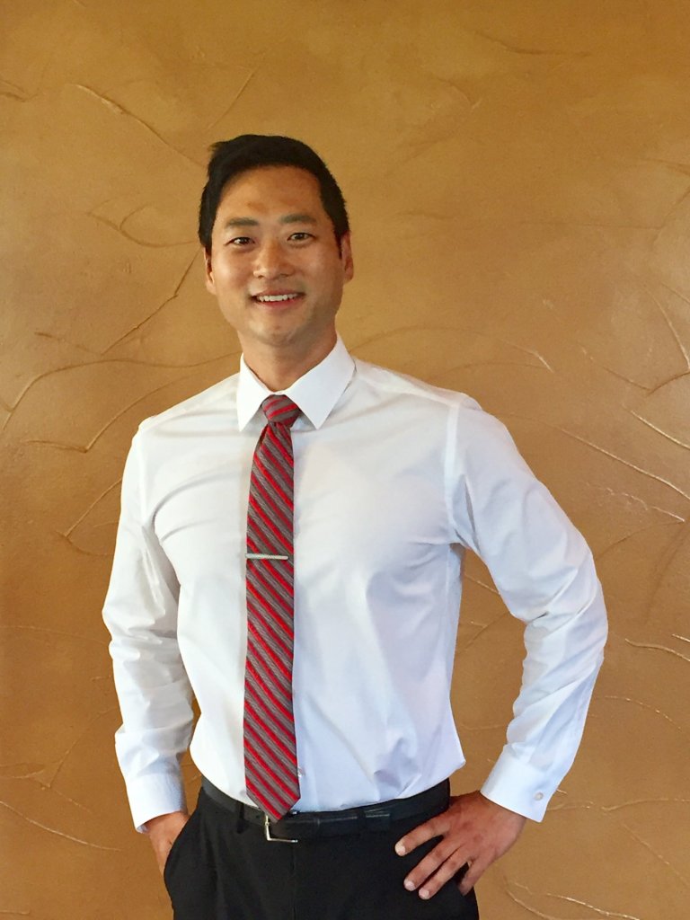 Dr. Douglas Hong wearing formal attire in front of a brown backdrop.