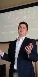 April Meeting, a member speaking in front of a projector screen.